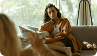 A client sits on a couch speaking with a therapist and they are wondering about what therapist abbreviations and psychologist abbreviations stand for