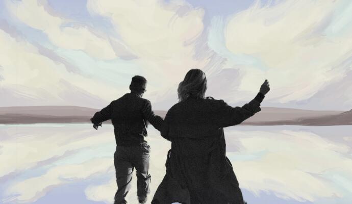 A silhouette of a couple in front of a blue, grey, and lilac sunset.
