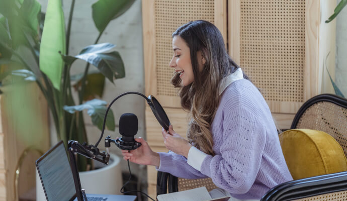 A woman sits in front of a laptop holding a recording mic.