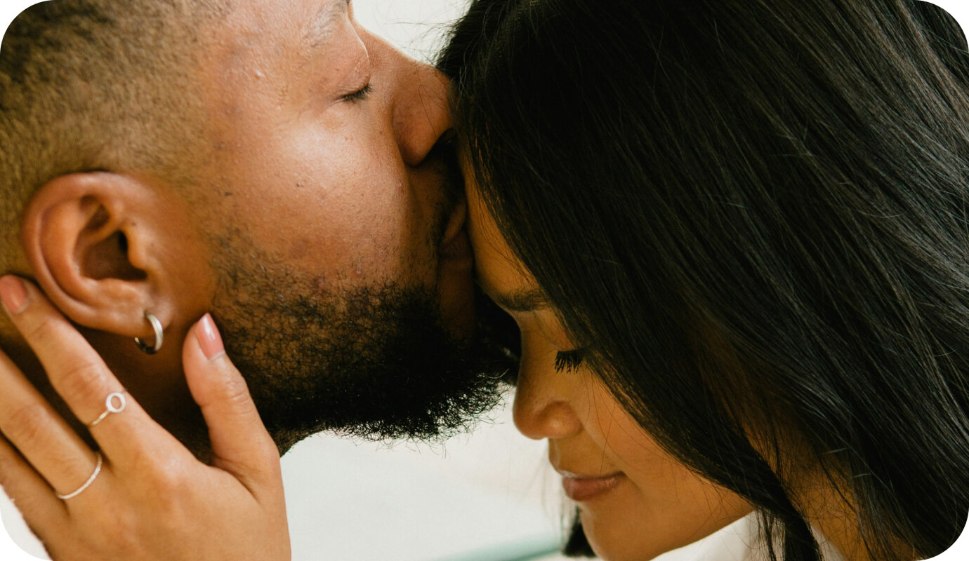 A couple in an embrace practices closeness and intimacy, key factors to making relationships last. One partner kisses the other on the forehead while she holds his neck.