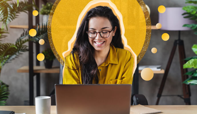 A woman is sitting at a desk looking at a laptop and smiling. There is a yellow decorative circle behind her.