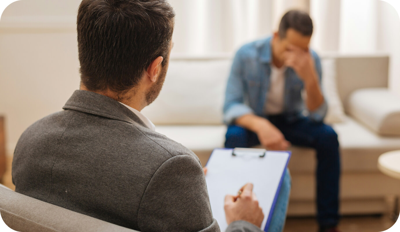 A therapist faces his distressed client. As he writes his session notes he also looks at the client and uses self-disclosure in therapy to show empathy and understanding for the client. There are many benefits and risks to self-disclosure in therapy. In this article, we share examples and ethical considerations for therapist self-disclosure.