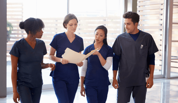 Four people in dark scrubs stand together looking at a folder.