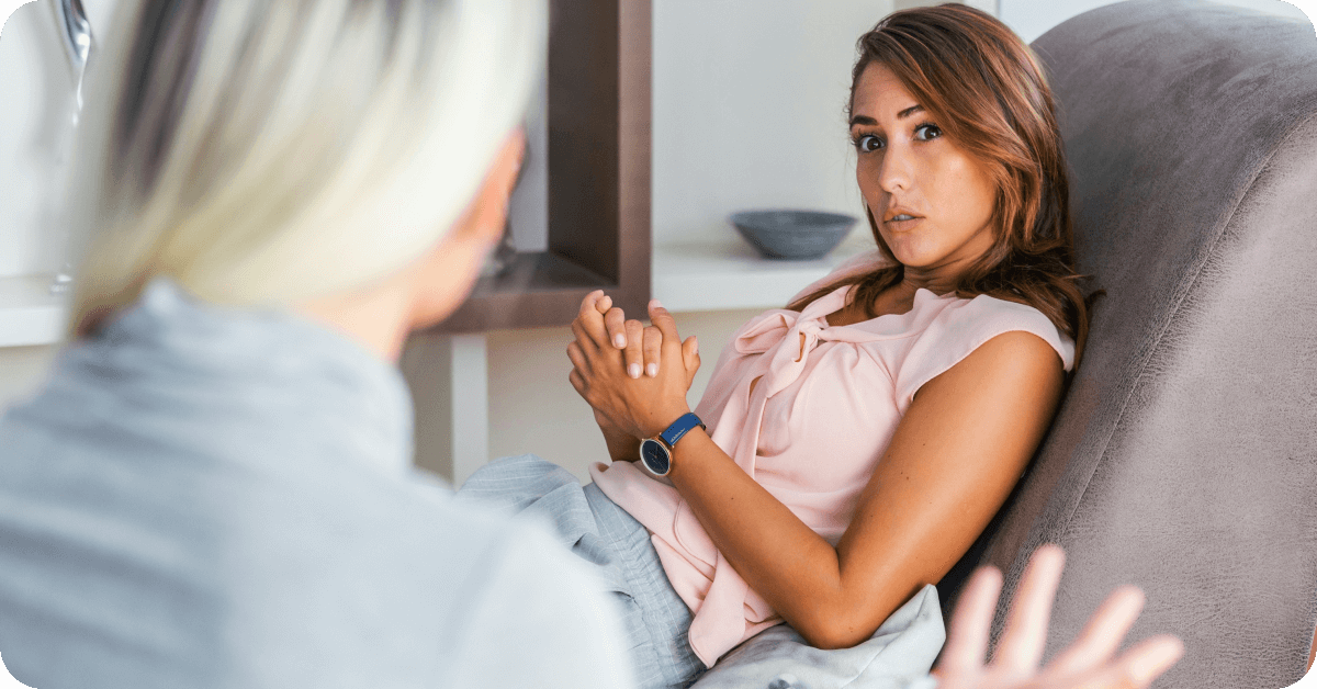 A client in distress clamps her hands, while the therapist explains a person-centered therapy techniques that may help.