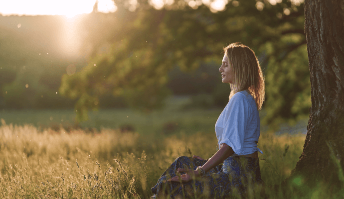 A woman sits under a tree outside, using her between-session minutes to meditate.